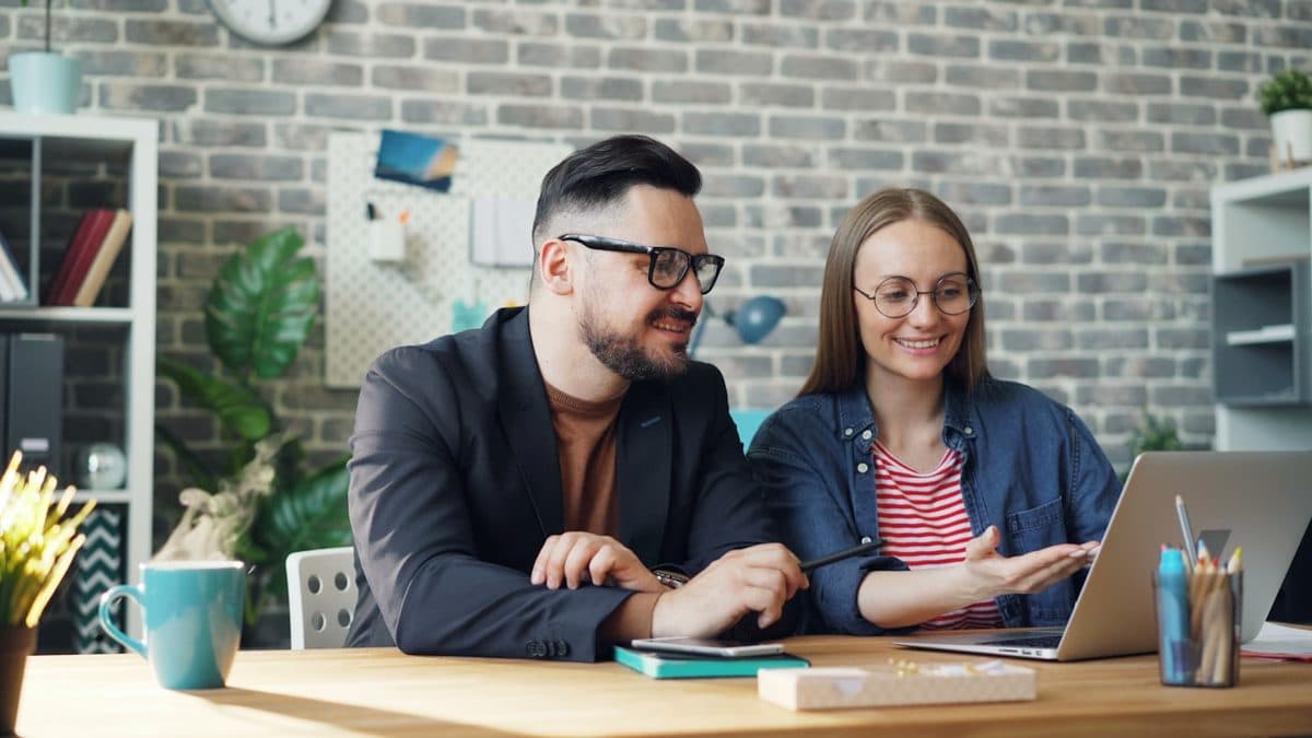 Two colleagues smiling as they work together at a laptop